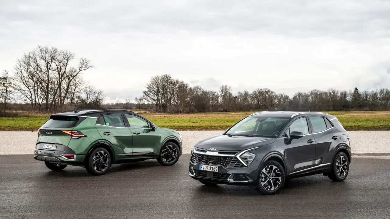 Dwa nowoczesne crossovery Kia Sportage, zielony i grafitowy, stoją na mokrej drodze na tle jesiennego krajobrazu.