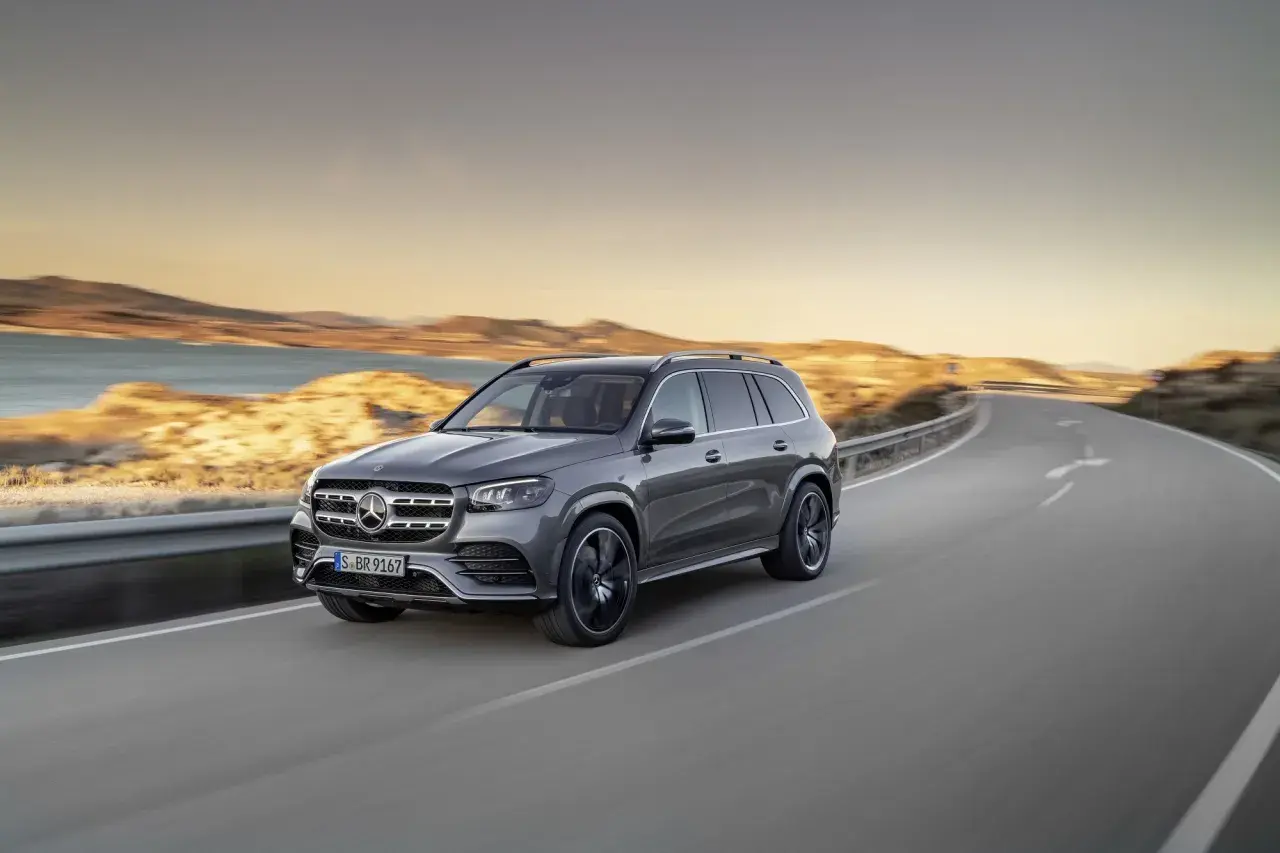Szary Mercedes GLS 580 sunie po krętej drodze nad brzegiem morza podczas zachodu słońca.