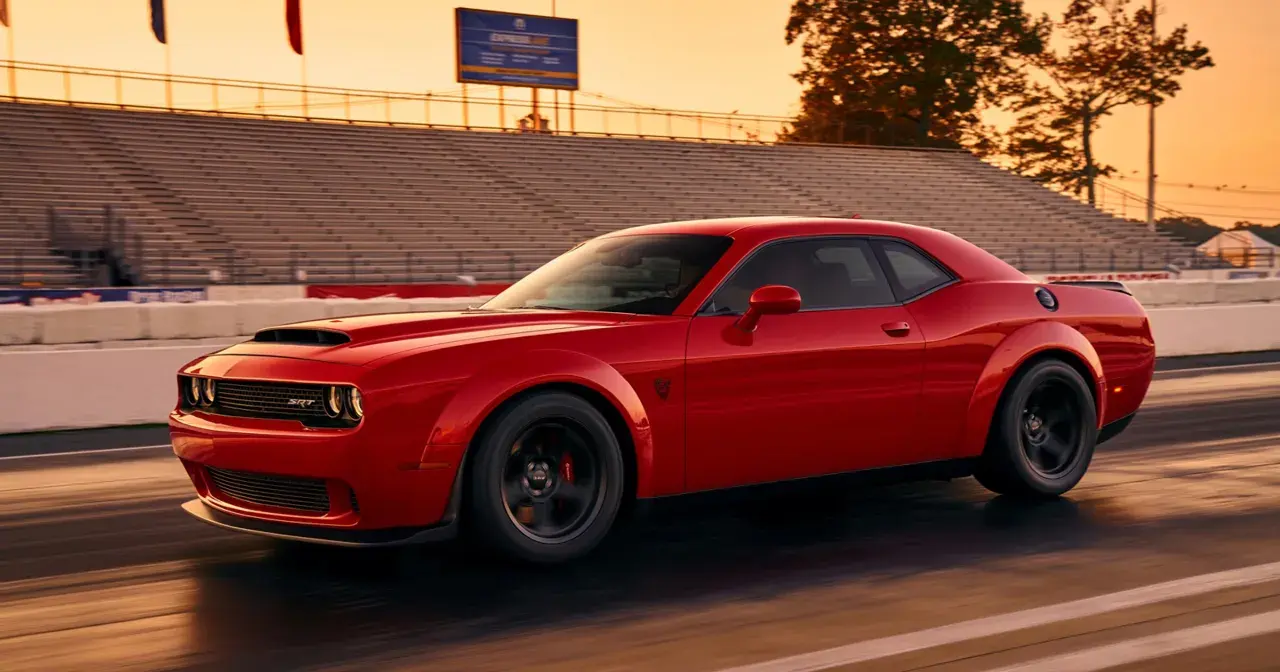 Czerwony Dodge Demon pędzi po torze wyścigowym podczas zachodu słońca, z trybunami w tle.