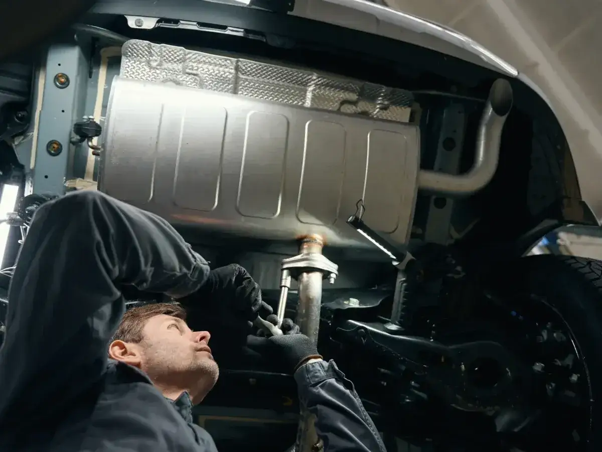 Mechanik pracuje pod samochodem, naprawiając układ wydechowy. Widoczny jest tłumik i rury. Kod p0420 może oznaczać problem z katalizatorem.