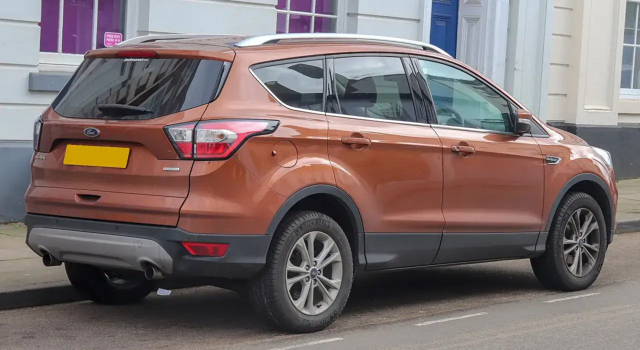 Pomarańczowy Ford Kuga, często chwalony w ford kuga opinie, zaparkowany przy budynku.