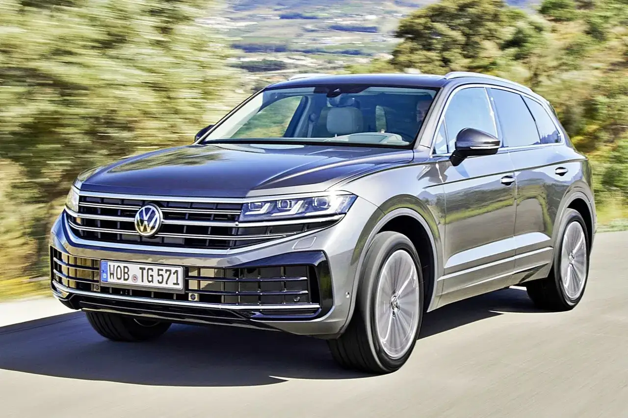 Szary Volkswagen Touareg 2024 pędzi po drodze, otoczony rozmytą zielenią krajobrazu.