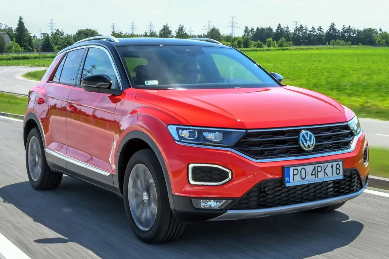 Czerwony volkswagen t-roc używany na drodze, z zielonym polem i liniami energetycznymi w tle.