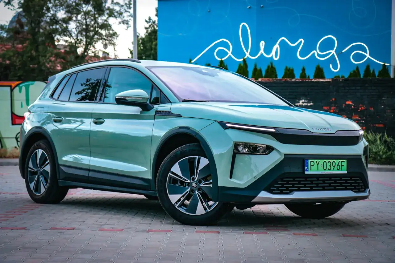 Nowy, zielony Skoda Elroq na tle niebieskiej ściany z neonowym napisem.
