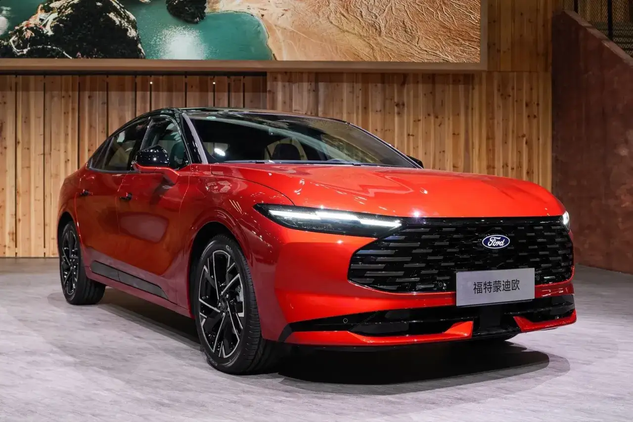Nowy Ford Mondeo 2025 w ognistym kolorze prezentuje się dynamicznie na tle drewnianej ściany.