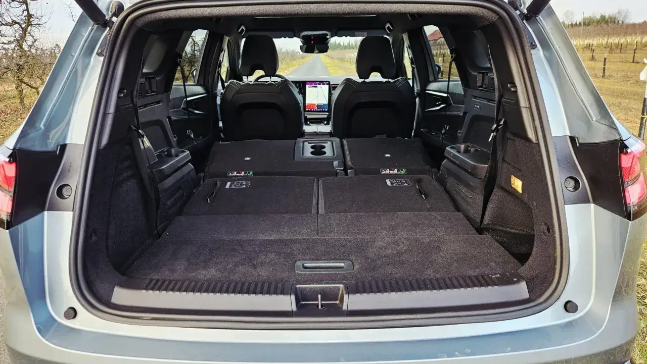 Wnętrze Renault Espace 2024 z rozłożonymi siedzeniami, tworzącymi dużą przestrzeń bagażową. Widok z tyłu na drogę.