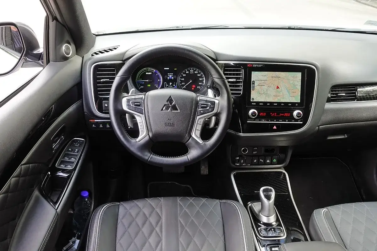 Wnętrze Mitsubishi Outlander 3 z ekranem nawigacji, kierownicą i wygodnymi, pikowanymi fotelami.