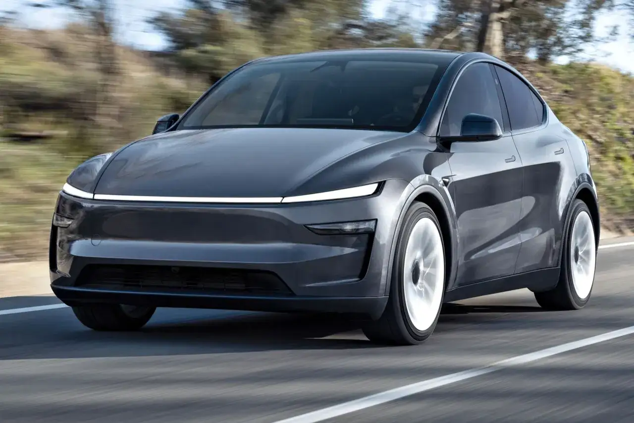 Szary Tesla Y 2025 pędzi po drodze, otoczony rozmytą zielenią.