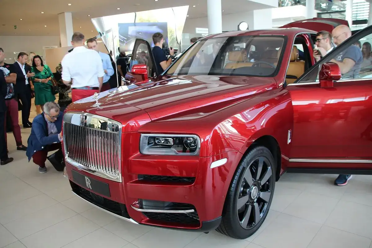 Czerwony Rolls-Royce Cullinan, marka samochodu na l, błyszczy w salonie. Ludzie oglądają luksusowy pojazd.