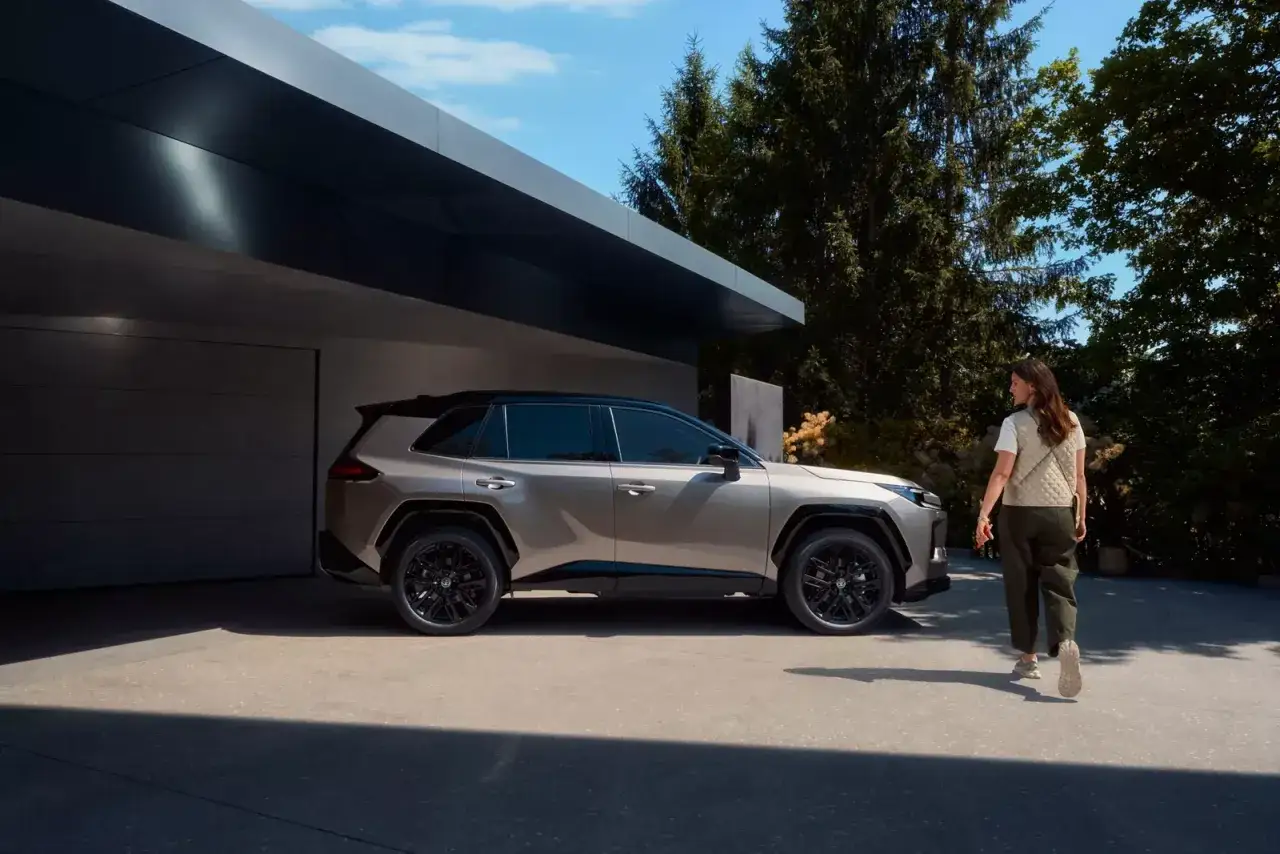 Elegancka kobieta zbliża się do nowego Toyota RAV4 2025 zaparkowanego przed nowoczesnym domem.