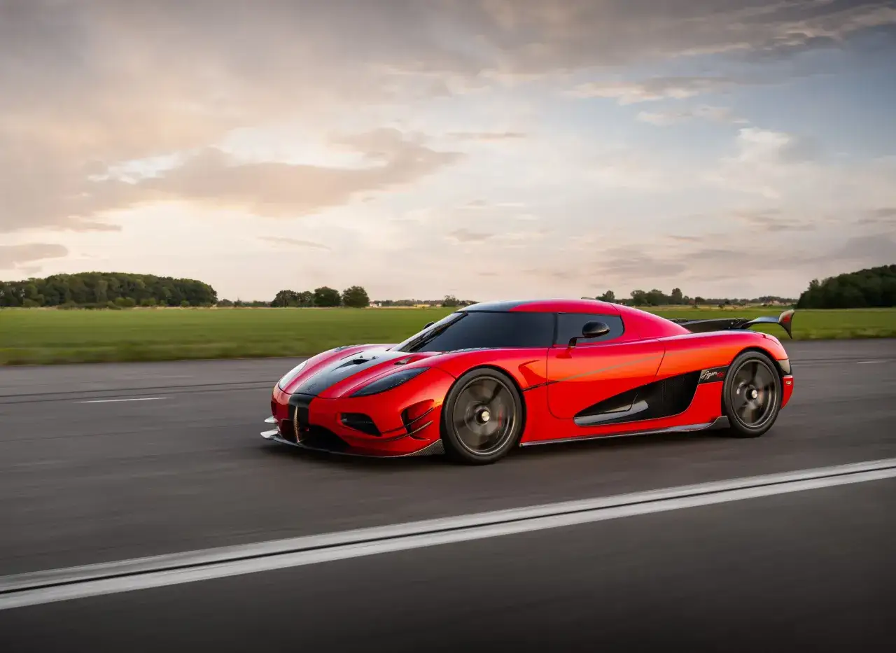 Czerwony Koenigsegg Agera RS pędzi po asfalcie, otoczony zielonymi polami i malowniczym niebem o zachodzie słońca.