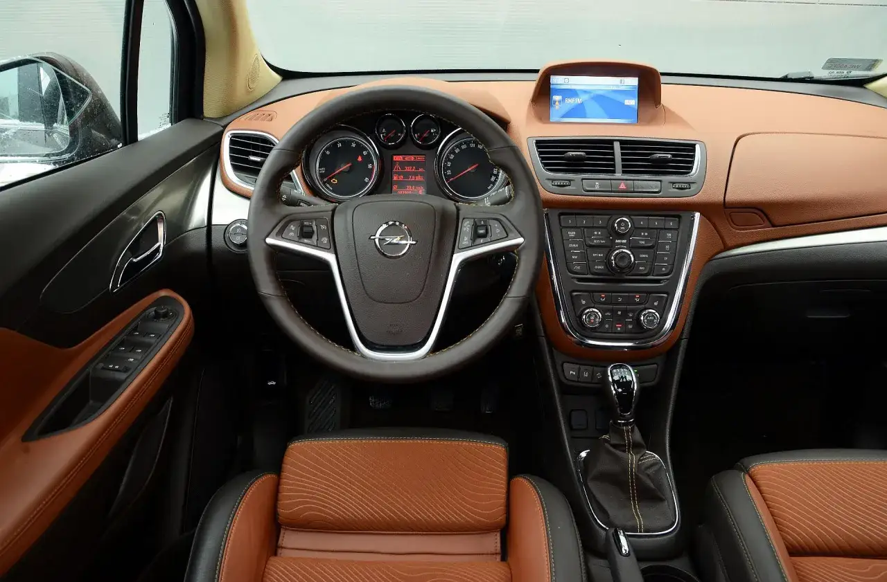 Wnętrze Opla Mokka 2015 z brązową tapicerką i ekranem multimedialnym.