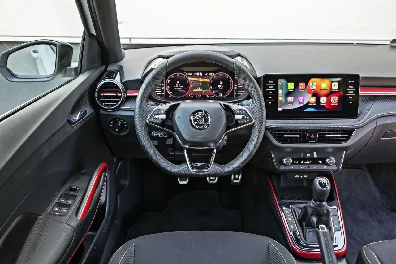 Wnętrze Skoda Fabia 2026: cyfrowe zegary, ekran multimediów z ikonami aplikacji, kierownica i dźwignia zmiany biegów.