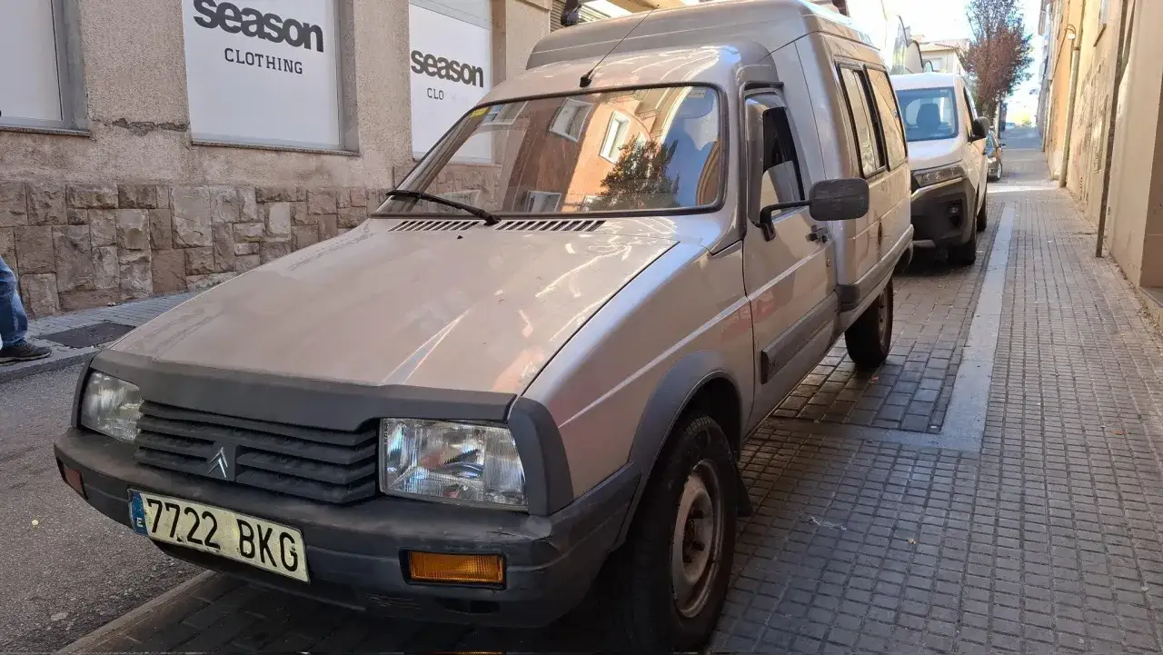 Klasyczny Citroen C15 w kolorze beżowym zaparkowany na wąskiej uliczce.