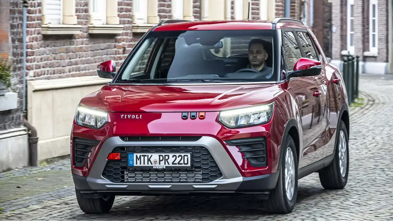 Czerwony SsangYong Tivoli z mężczyzną za kierownicą jedzie brukowaną uliczką.