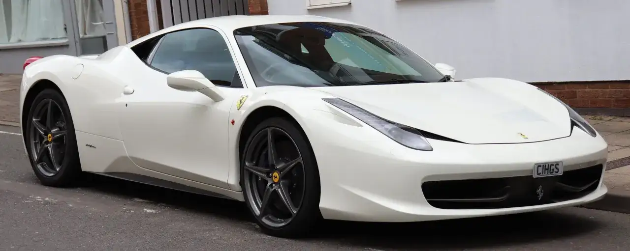 Białe Ferrari 458 Italia, lśniące na ulicy, z charakterystycznym logo i felgami.