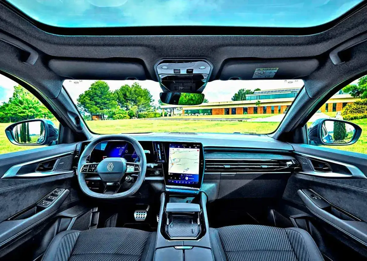 Wnętrze Renault Austral 2025 z panoramicznym dachem i nowoczesnym ekranem multimedialnym. Widok na zielony krajobraz.