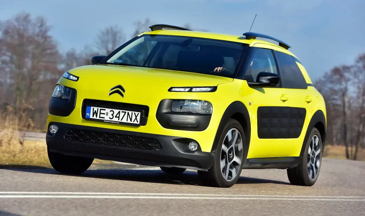 Żółty Citroen Cactus z czarnymi wstawkami i relingami na dachu jedzie po drodze.