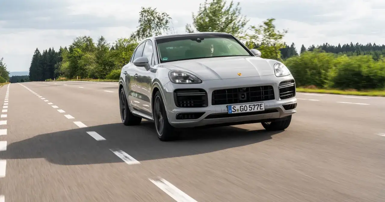 Szary Porsche Cayenne 2025 sunie po asfaltowej drodze, otoczony zielenią lasów.