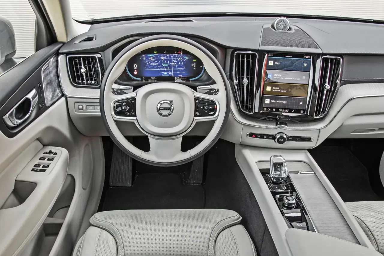 Wnętrze Volvo XC60 z ekranem nawigacji i multimediów. Kierownica z przyciskami, jasna tapicerka. Wiele osób szuka volvo xc60 opinie przed zakupem.