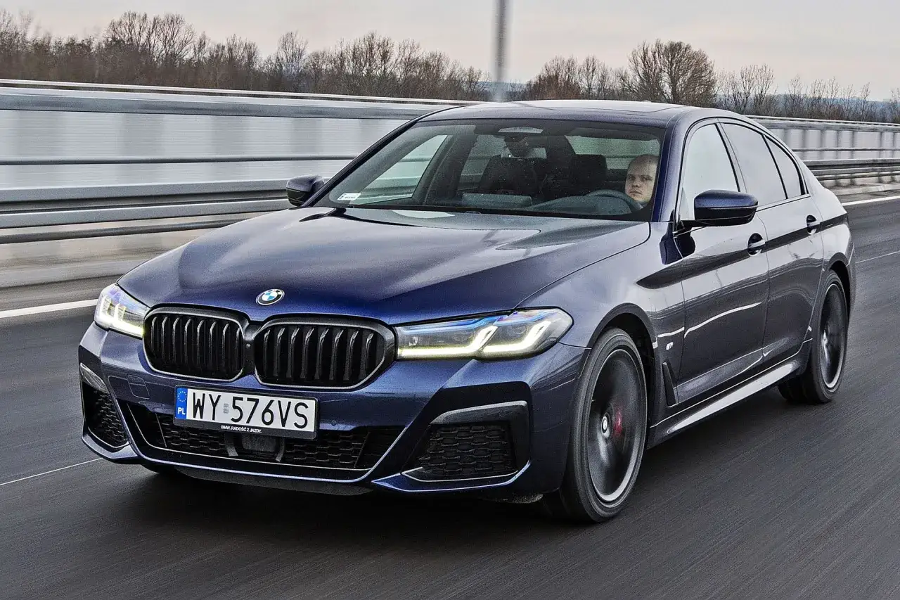 Ciemnoniebieskie BMW 520d xDrive jedzie autostradą. Kierowca z zaciekawieniem obserwuje drogę.