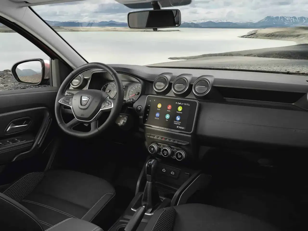 Wnętrze nowej Dacii Duster z ekranem multimediów i widokiem na jezioro i góry.