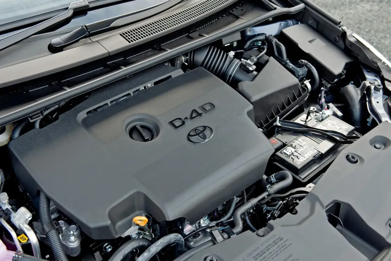 Silnik Toyota Avensis 2.0 D4D. Widoczny jest plastikowy dekiel silnika z logo Toyoty i oznaczeniem D-4D, a także akumulator.
