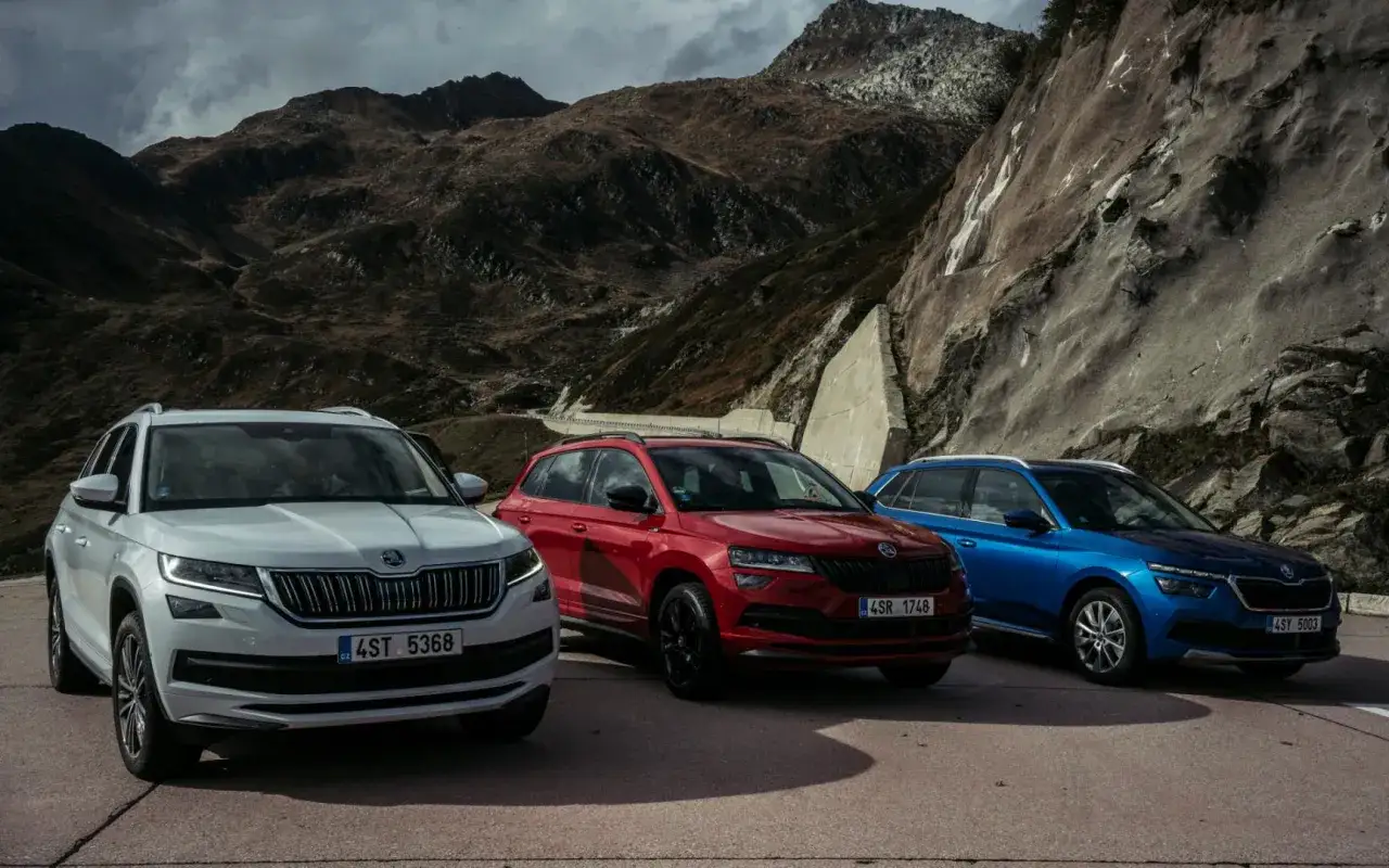 Trzy Skoda SUV: biały, czerwony i niebieski, zaparkowane na tle górskiego krajobrazu.