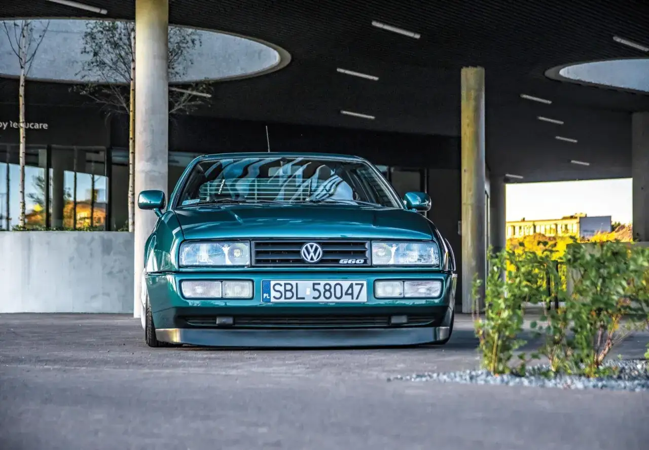 Zielony Volkswagen Corrado G60 z obniżonym zawieszeniem, zaparkowany pod nowoczesnym budynkiem.