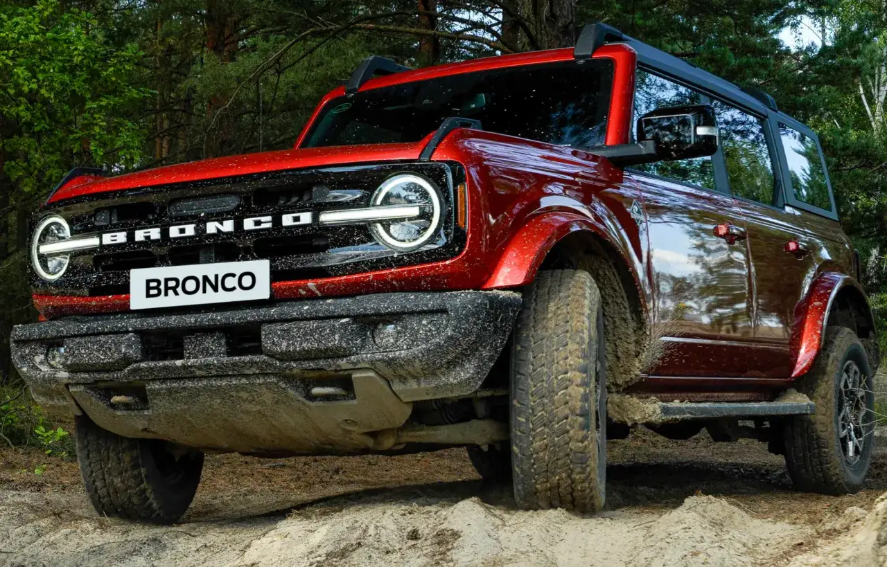 Czerwony Bronco w błocie, gotowy na przygodę w lesie.