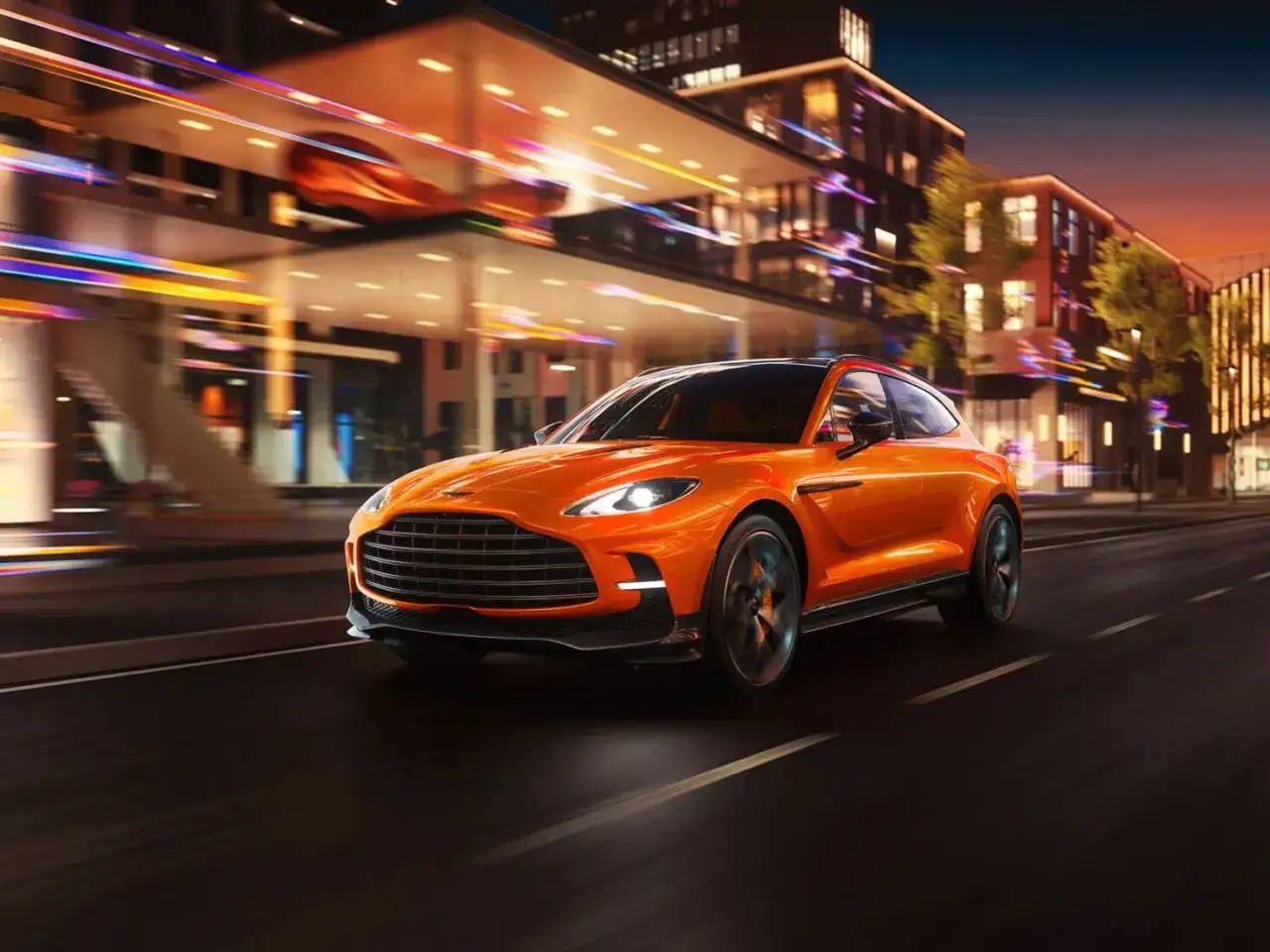 Pomarańczowy Aston Martin SUV pędzi nocą przez miasto, rozświetlone neonami budynków.