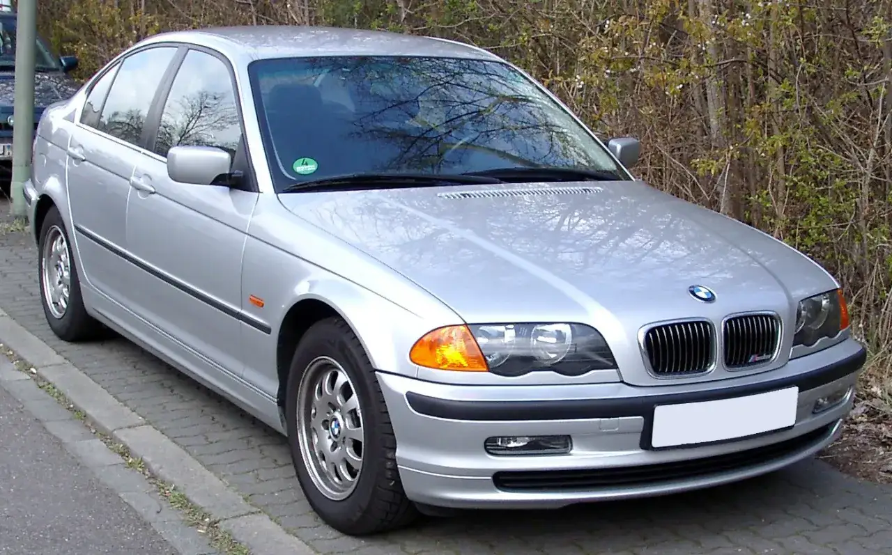 Srebrne BMW 325i stoi na chodniku, otoczone krzewami.
