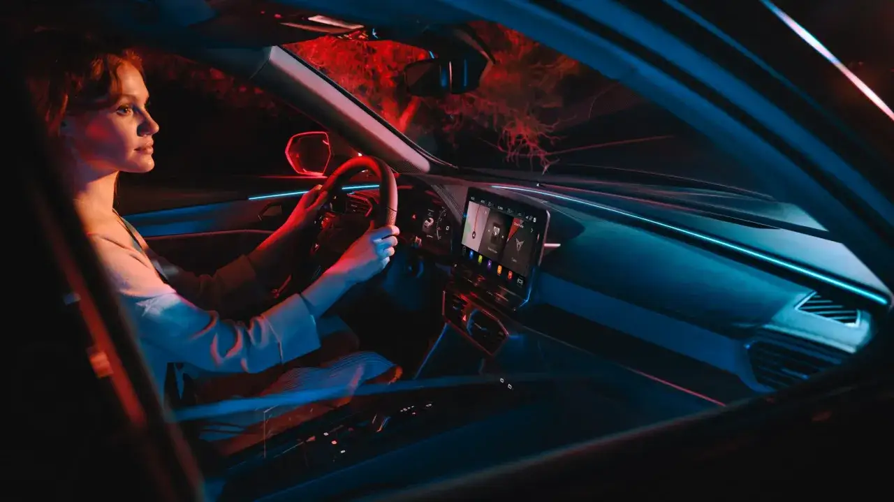 Kobieta za kierownicą Formentor Cupra, nocna jazda w otoczeniu neonowego światła.