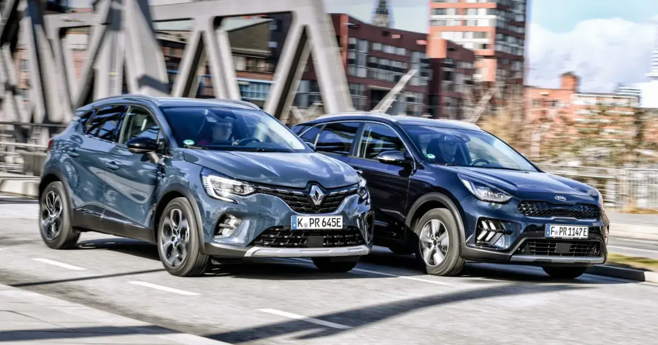 Dwa SUV-y, jeden szary Renault, drugi ciemnoniebieski Kia Niro, jadą obok siebie po miejskiej drodze.