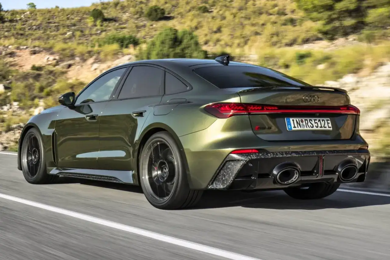 Nowy Audi RS5 2026 w kolorze oliwkowym pędzi po krętej drodze, prezentując sportowy tył z czterema końcówkami wydechu.