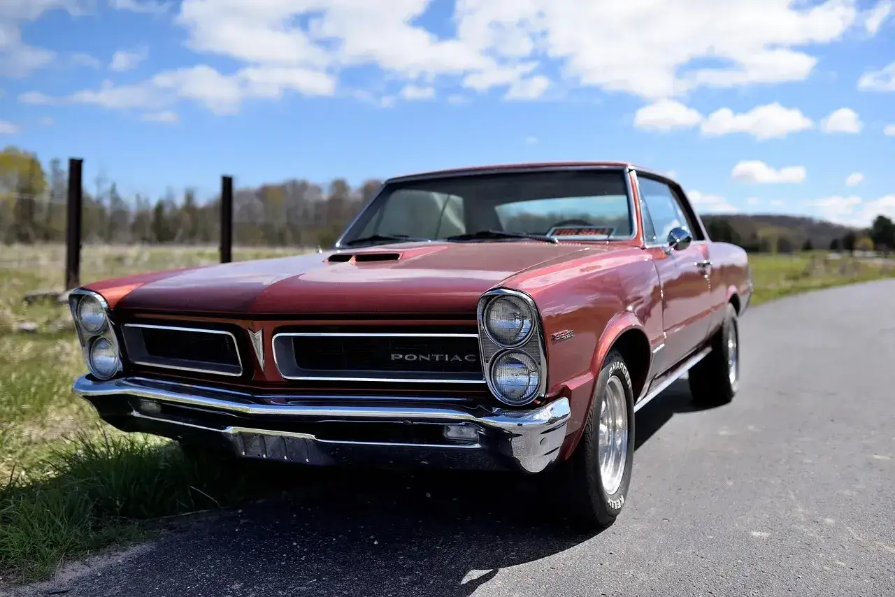 Klasyczny, czerwony Pontiac GTO na sprzedaż, zaparkowany na poboczu drogi w słoneczny dzień.
