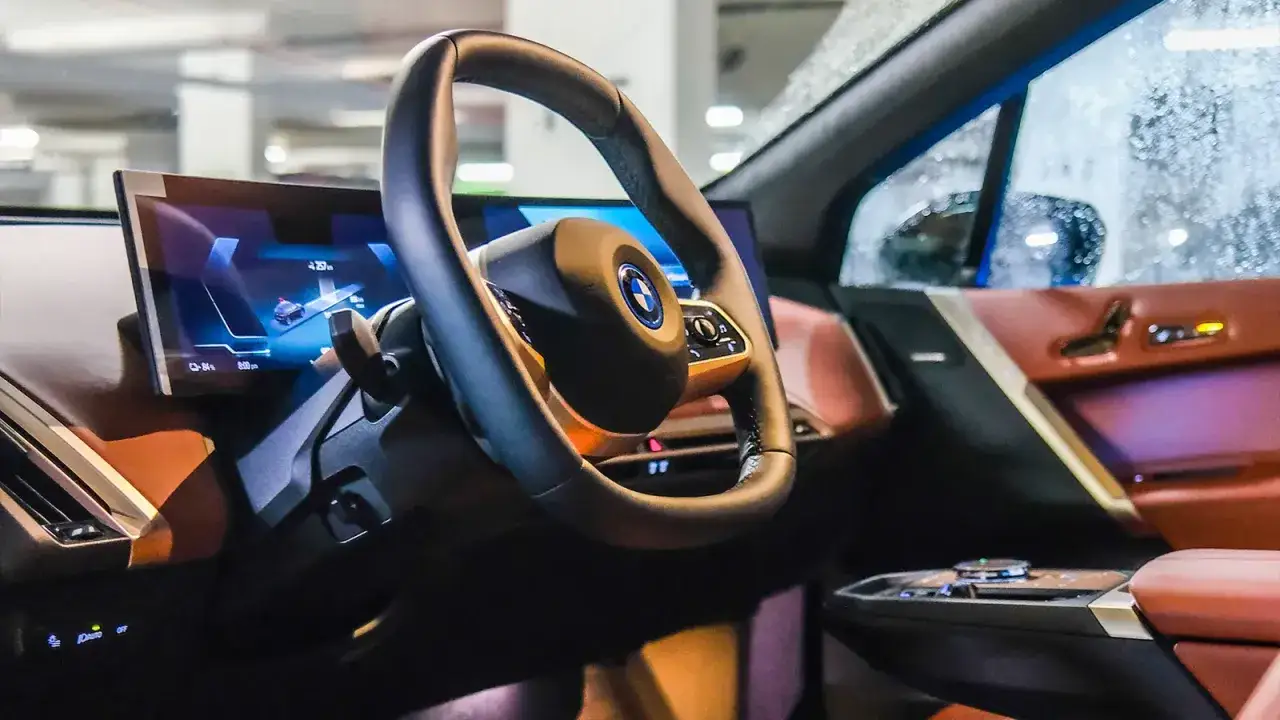 Wnętrze BMW iX z nowoczesnym ekranem i kierownicą. Skórzana tapicerka w odcieniach brązu i fioletu.