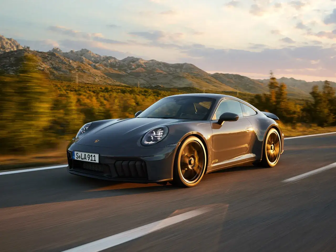 Szary Porsche 911 GTS na drodze wśród gór. Sprawdź aktualną porsche 911 cena.