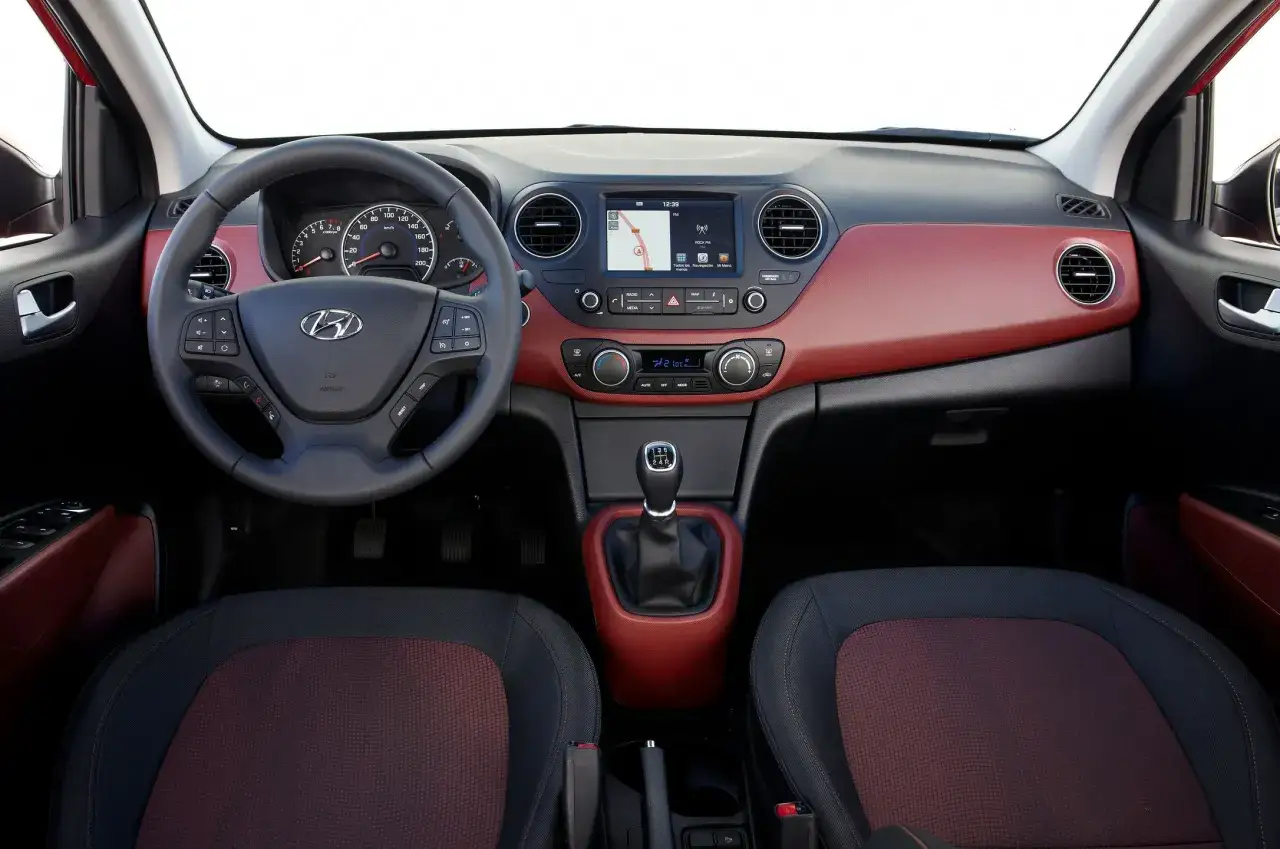 Wnętrze Hyundai i10 z czerwoną tapicerką, ekranem nawigacji i manualną skrzynią biegów.