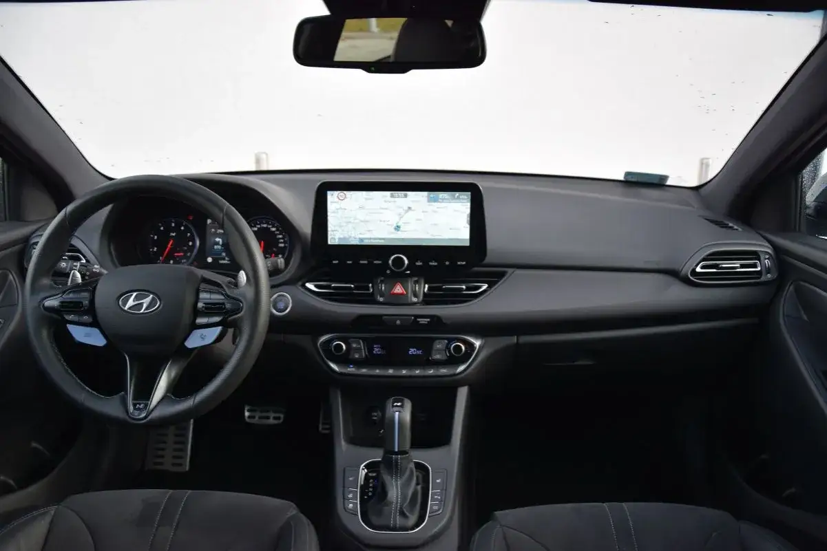Wnętrze Hyundai i30 2024: kierownica, ekran multimedialny z nawigacją, cyfrowe zegary i automatyczna skrzynia biegów.