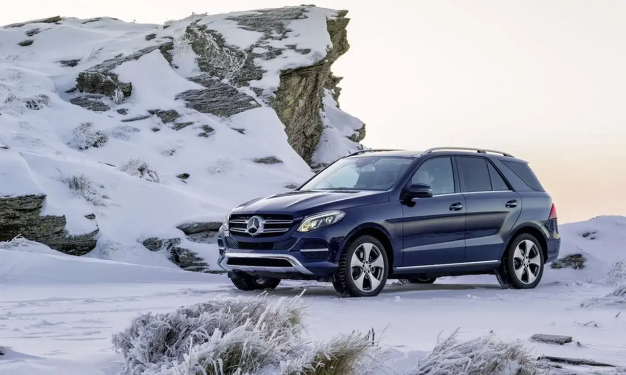 Ciemnoniebieski Mercedes 4x4 na tle ośnieżonych skał i mroźnej roślinności.