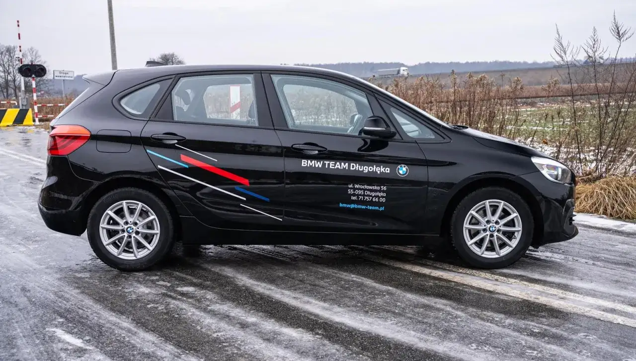 Czarne BMW F45 z logo BMW TEAM Długołęka na drzwiach, stoi na oblodzonej drodze.