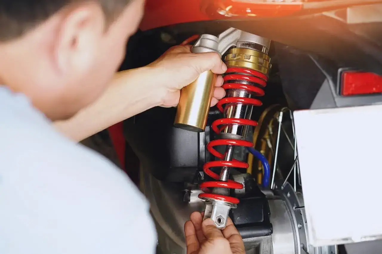 Mechanik reguluje amortyzator w motocyklu. Czerwona sprężyna i złote elementy świadczą o wysokiej jakości zawieszenia.
