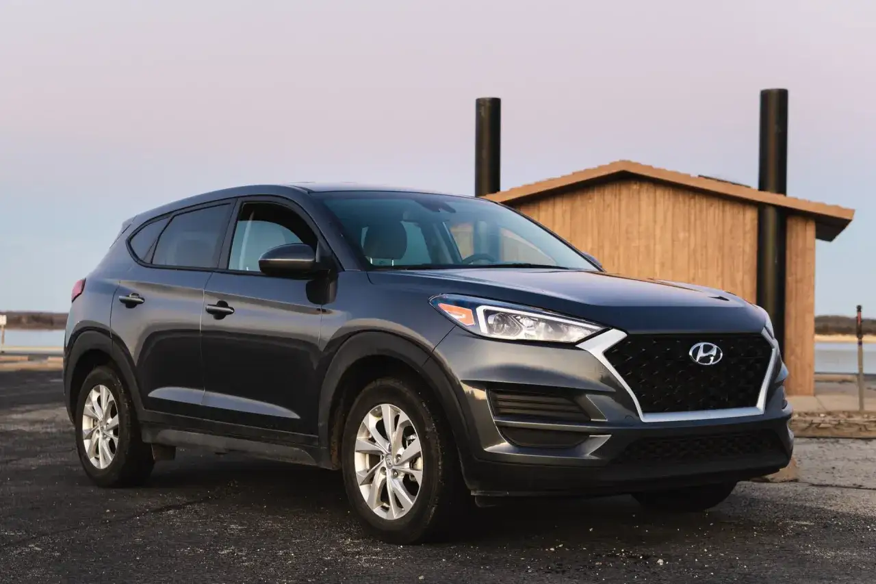 Ciemnoszary Hyundai Tucson 2016 zaparkowany przy drewnianej budce nad jeziorem.