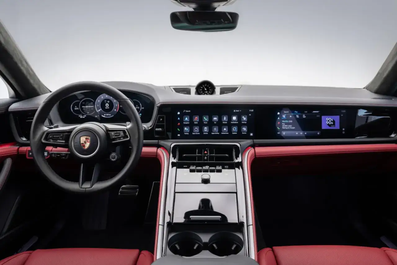 Wnętrze Porsche Panamera: kierownica, cyfrowe zegary, ekran multimediów z ikonami i radiem, czerwona skórzana tapicerka.