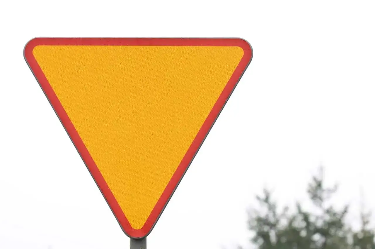 Żółty trójkąt z czerwoną obwódką, znak ustąp pierwszeństwa, ostrzega przed zbliżającym się skrzyżowaniem.