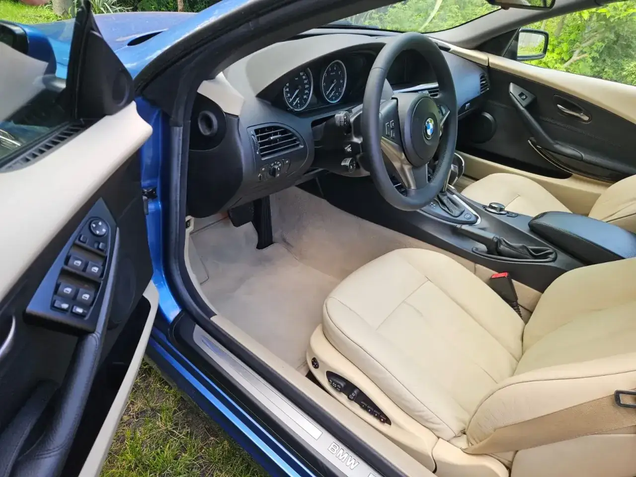 Wnętrze BMW E64 z jasną, skórzaną tapicerką i niebieskimi akcentami. Widok na deskę rozdzielczą, kierownicę i fotele.