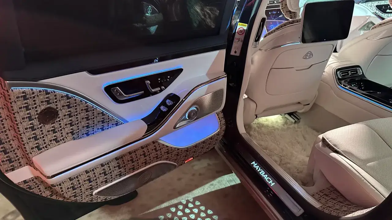 Wnętrze Maybach S680: biała skóra, ozdobne panele drzwi z tkaniny, niebieskie oświetlenie ambientowe i ekran multimedialny.