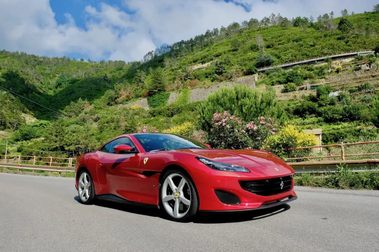 Czerwone Ferrari Portofino na tle zielonych wzgórz i błękitnego nieba. Idealne na przejażdżkę po malowniczej drodze.