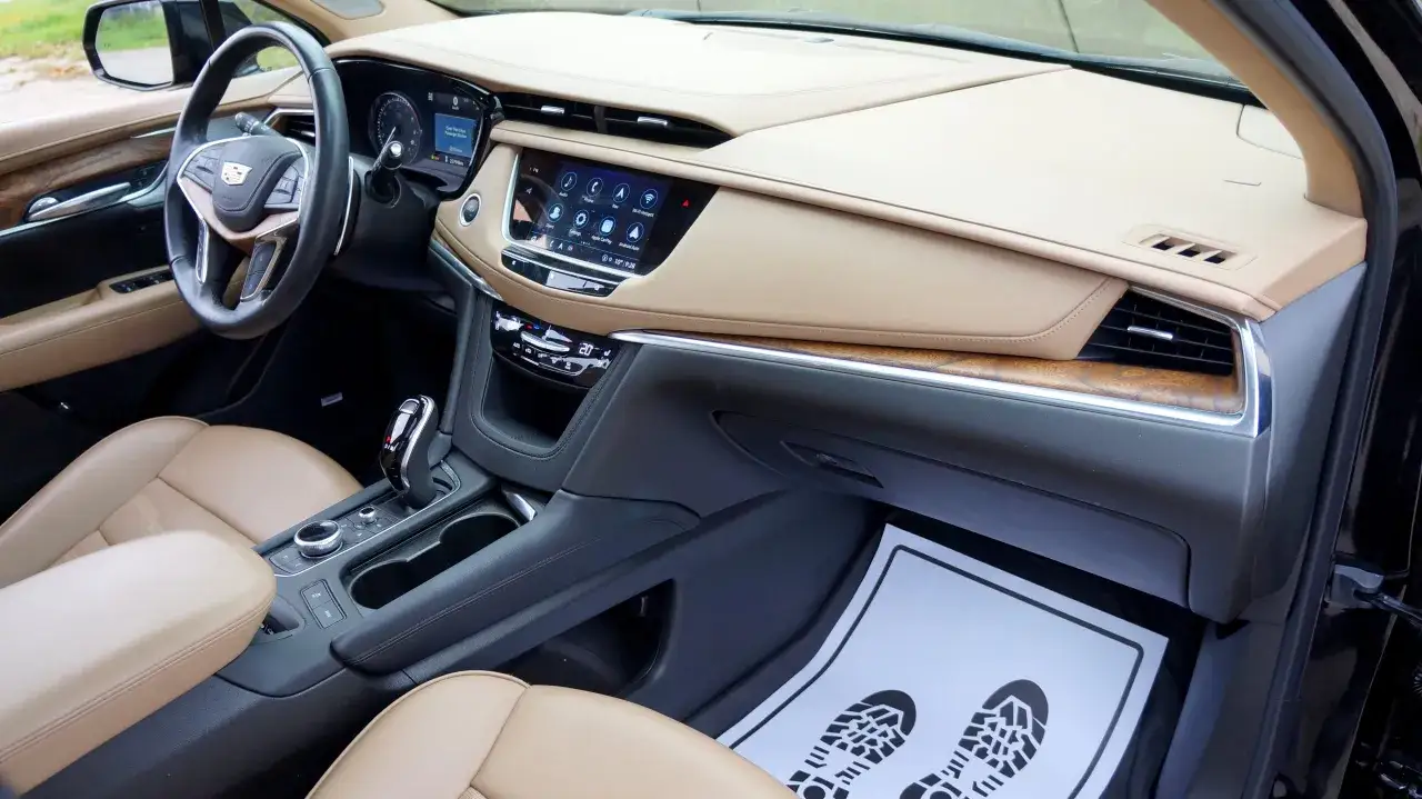 Wnętrze luksusowego Cadillac XT5 z beżową tapicerką, ekranem dotykowym i drewnianymi wstawkami.